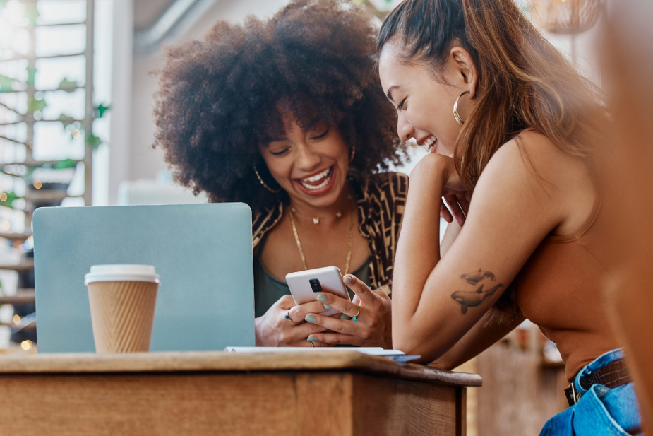 An image of two young women searching on their smartphones for new coffee shop locations